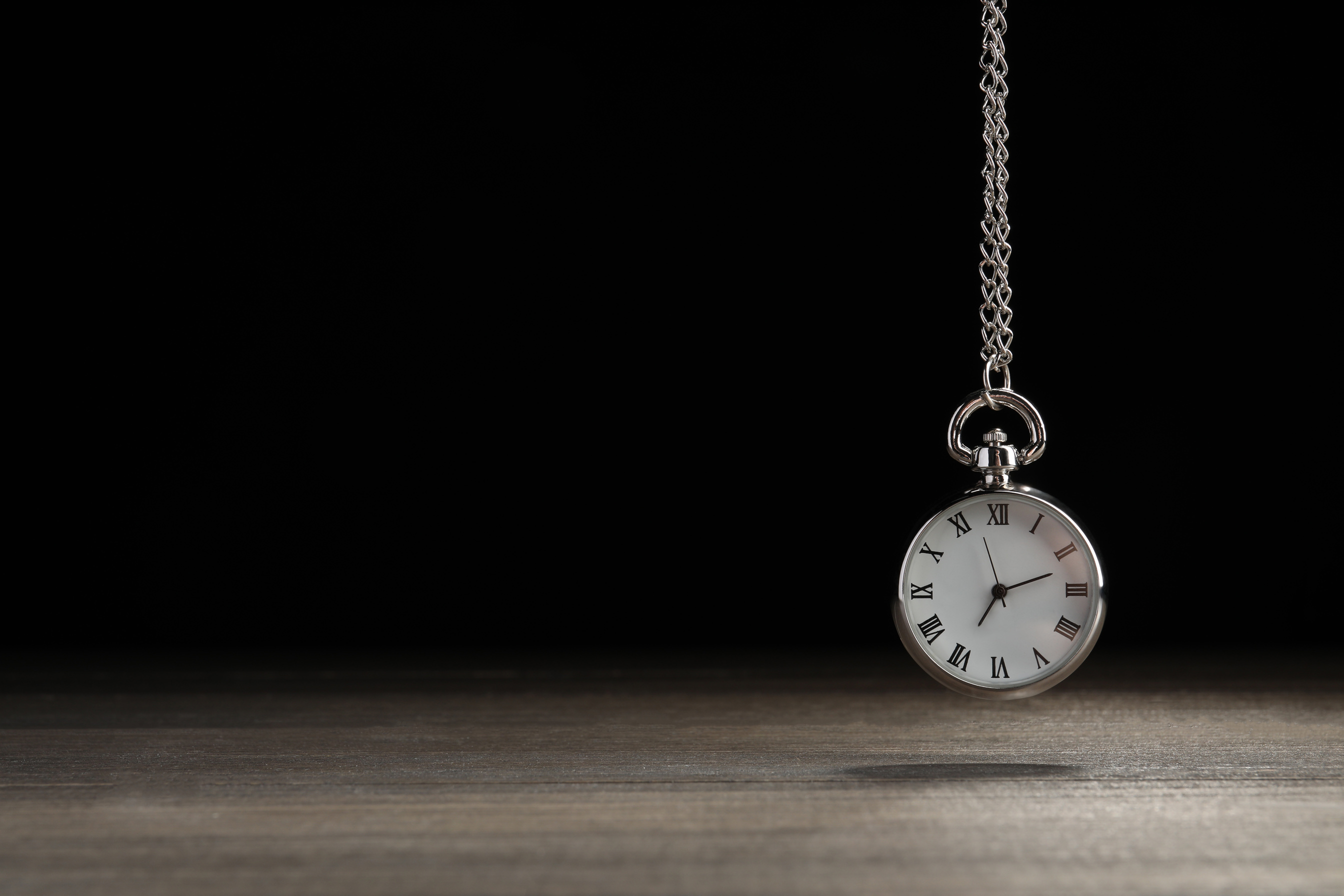Beautiful Vintage Pocket Watch with Silver Chain on Black Background above Wooden Table, Space for Text. Hypnosis Session